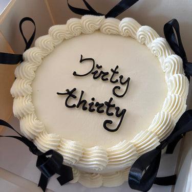 Кръгла бяла торта с надпис "Dirty thirty", украсена с панделки и кремав кант