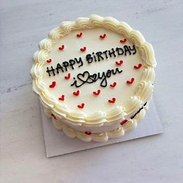 Round cream cake with a cream border, red hearts and the inscription HAPPY BiRTHDAY i ♥ you.