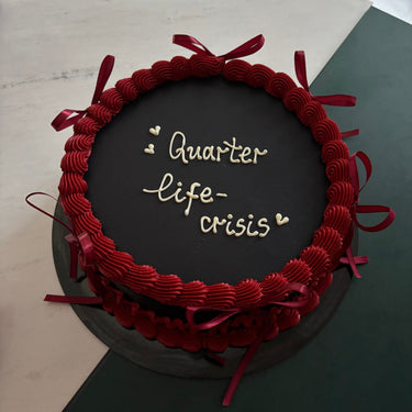 Кръгла черна торта с кремав кант и панделки, надпис 'Quarter life-crisis'