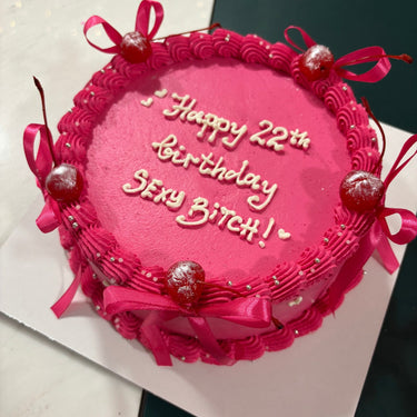 Кръгла розова торта с кремав кант, панделки, черешки и перли, с надпис Happy 22th Birthday SEXY BITCH!