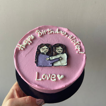 Кръгла розова торта с ръчна рисунка и надпис 'Happy Birthday, Sister! Love' със сърце.