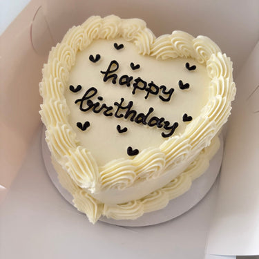 Кремава торта във форма на сърце с кремав кант и надпис 'happy birthday'.