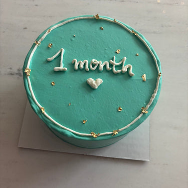 Round mint cake with glitter and gold details for the baby's first month.
