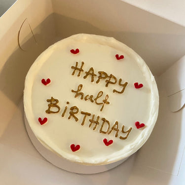Round white cake with the message Happy half BIRTHDAY in gold