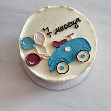 Кръгла бяла торта с рисунка на кола и балони за бебешка месечинка.
