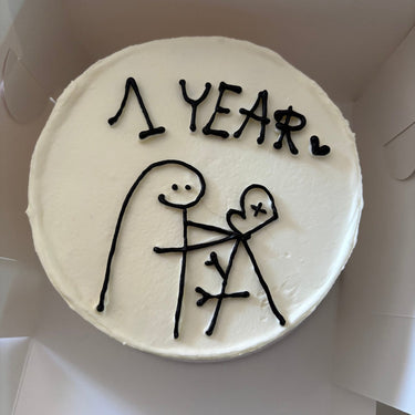Кръгла бяла торта с декоративна рисунка и надпис '1 YEAR.'