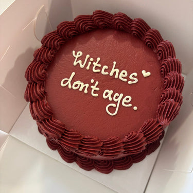 Кръгла бордо торта с кремав кант и надпис 'Witches don't age.'