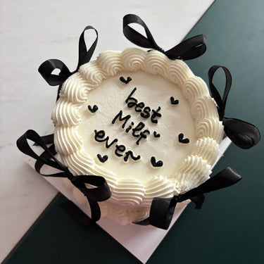 White round cake with ribbons and a cream border, inscription 'best Milf ever' on the icing.
