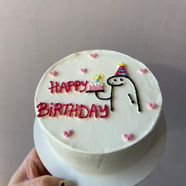 Кръгла бяла торта с нарисуван човек и надпис 'HAPPY BiRTHDAY' отгоре.