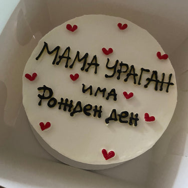 Кръгла бяла торта с надпис 'МАМА УРАГАН има Рожден ден' отгоре, без допълнителна украса.