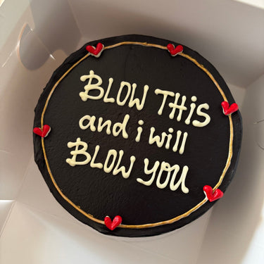 Кръгла черна торта с кремав кант и златен надпис 'BLOW THIS and i will BLOW you'