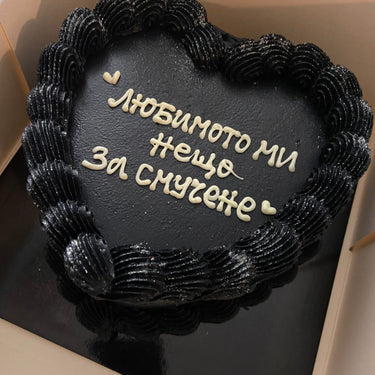 Сърцевидна черна торта с брокат, кремав кант и надпис 'любимото ми нещо за смучене'.
